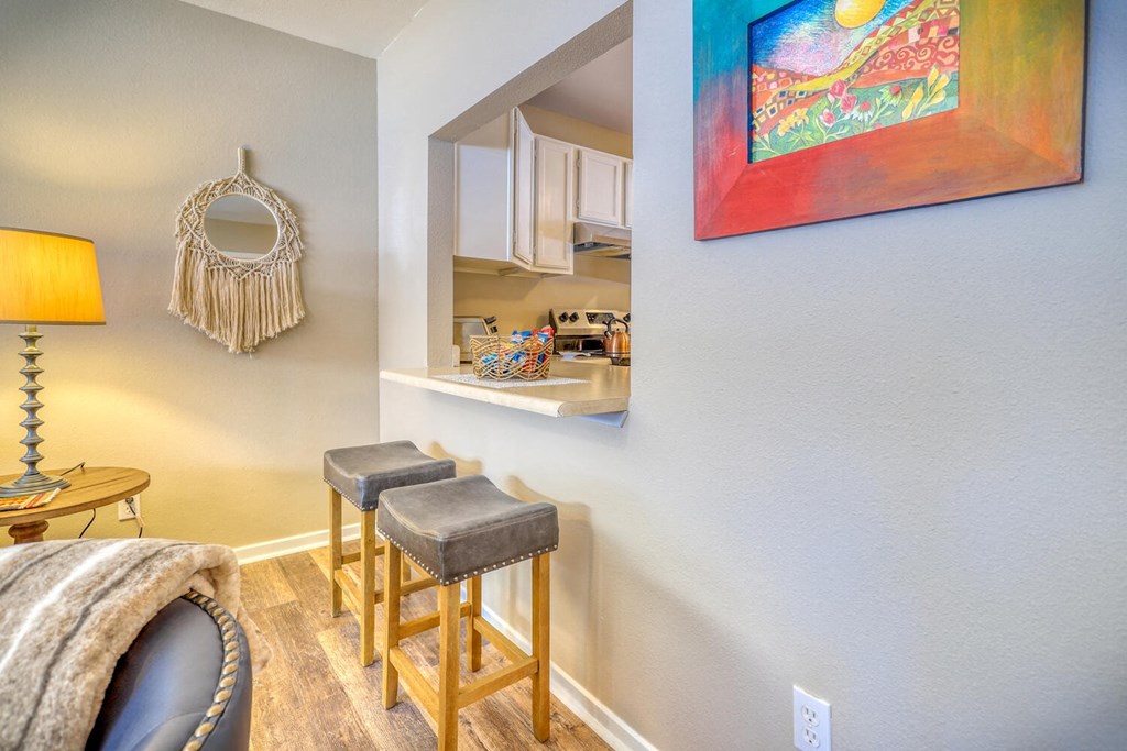 a living room with two bar stools and a kitchen with a mirror