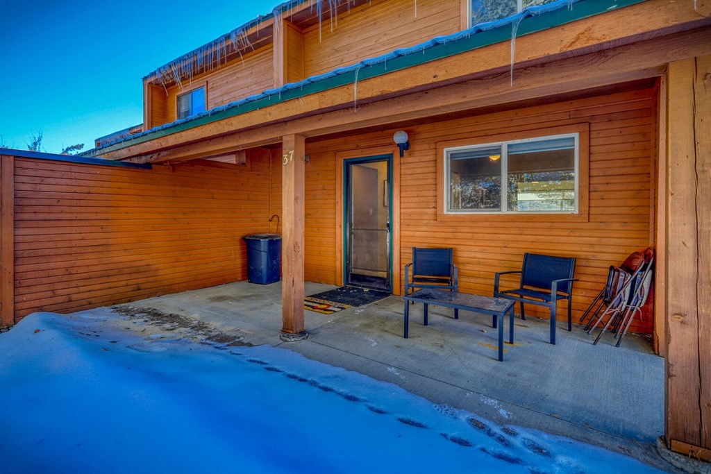 the front porch of a cabin with two chairs and a table