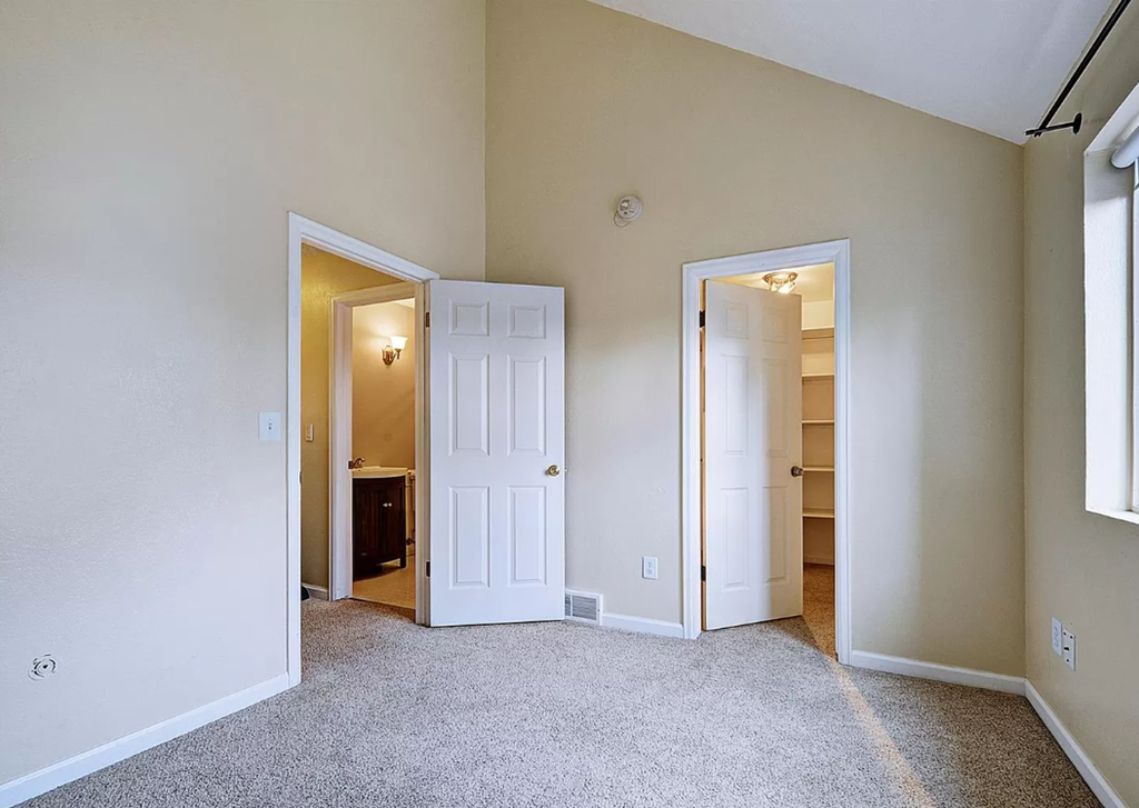 an empty bedroom with open doors to a bathroom and a closet