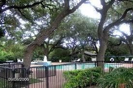 a fountain in a park with trees and a fence