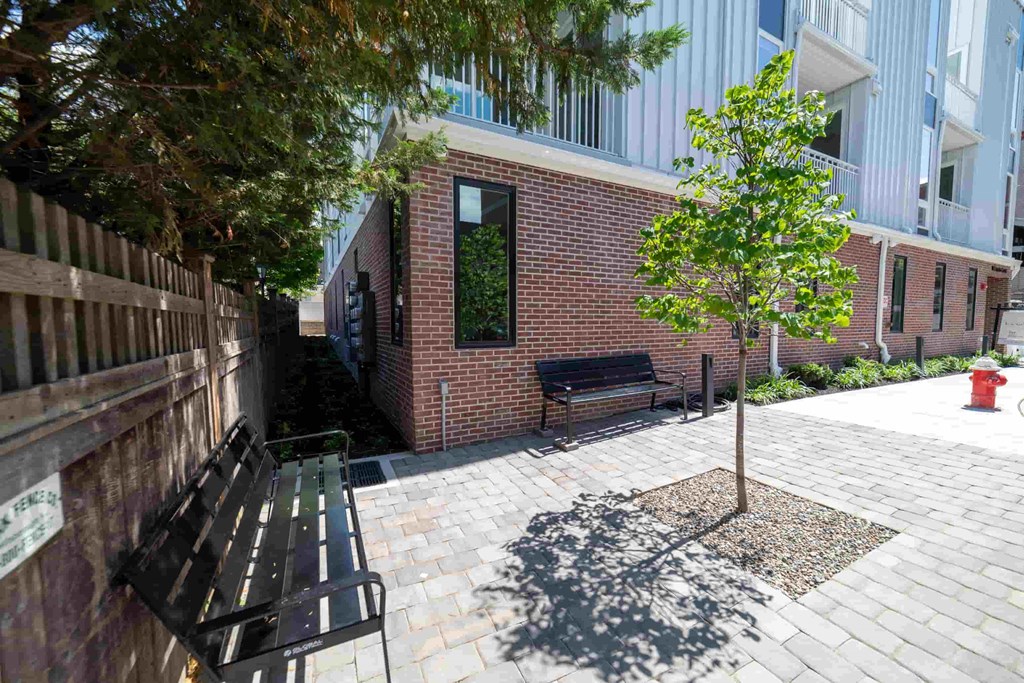 a courtyard with benches and a tree in front of a brick building
