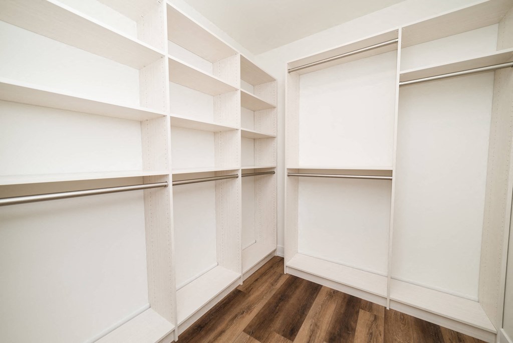 a walk in closet with white walls and wood floors