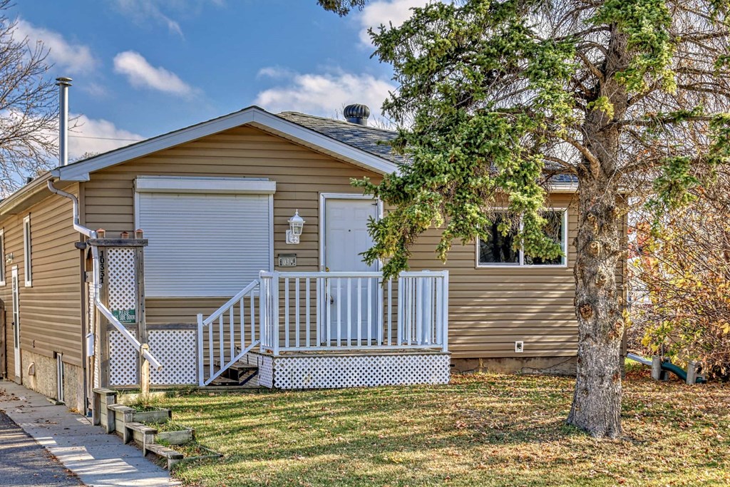the front of a yellow house with a porch and a tree