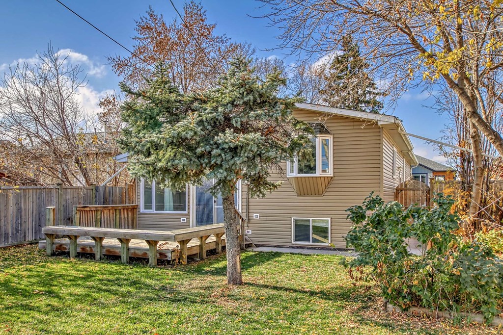 a yellow house with a wooden deck and a tree in front of it