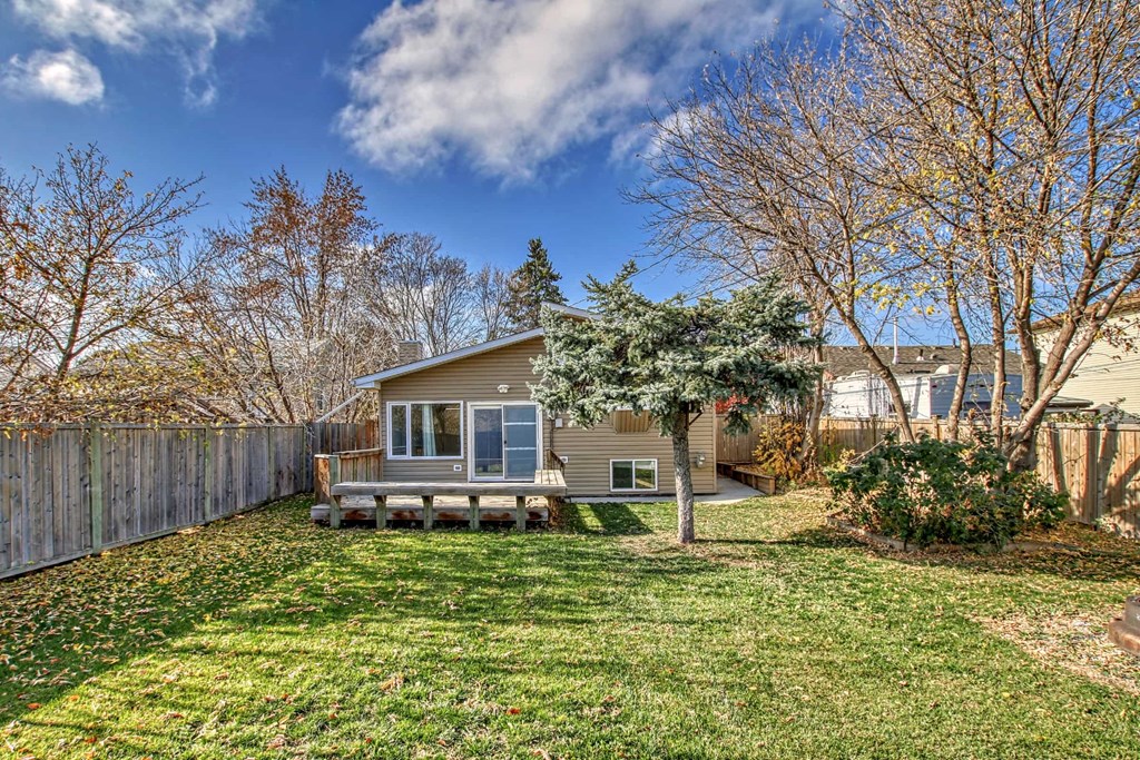 a small brown house with a yard and a wooden fence