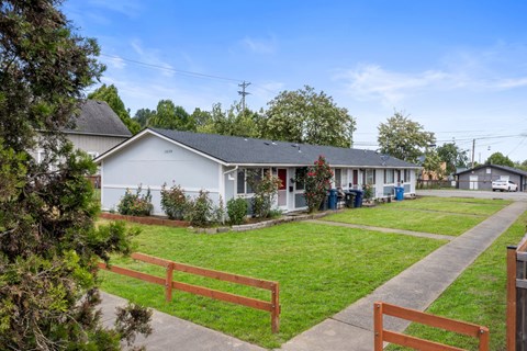the front yard of a white house with a lawn and a bench