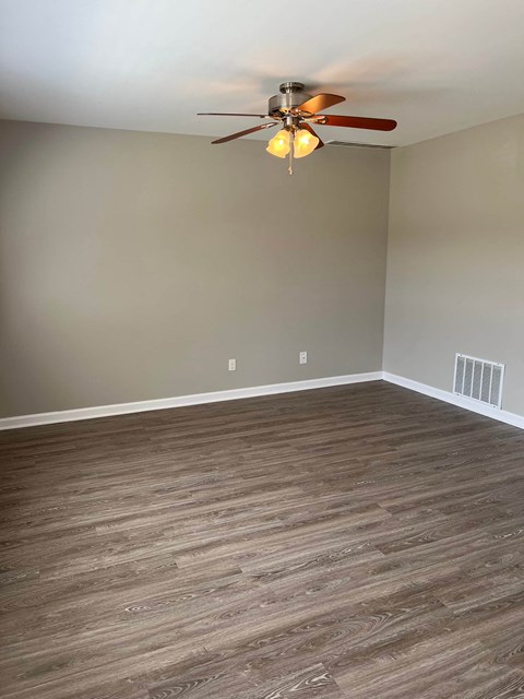an empty living room with wood floors and a ceiling fan