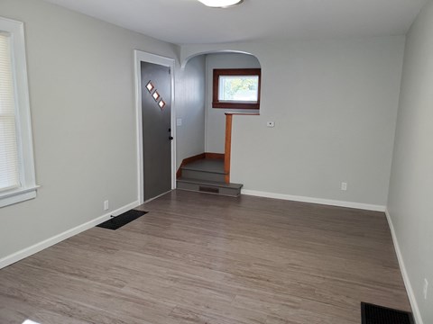 an empty living room with a hardwood floor and a door to a hall way