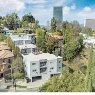 A modern white house is surrounded by trees and other houses.