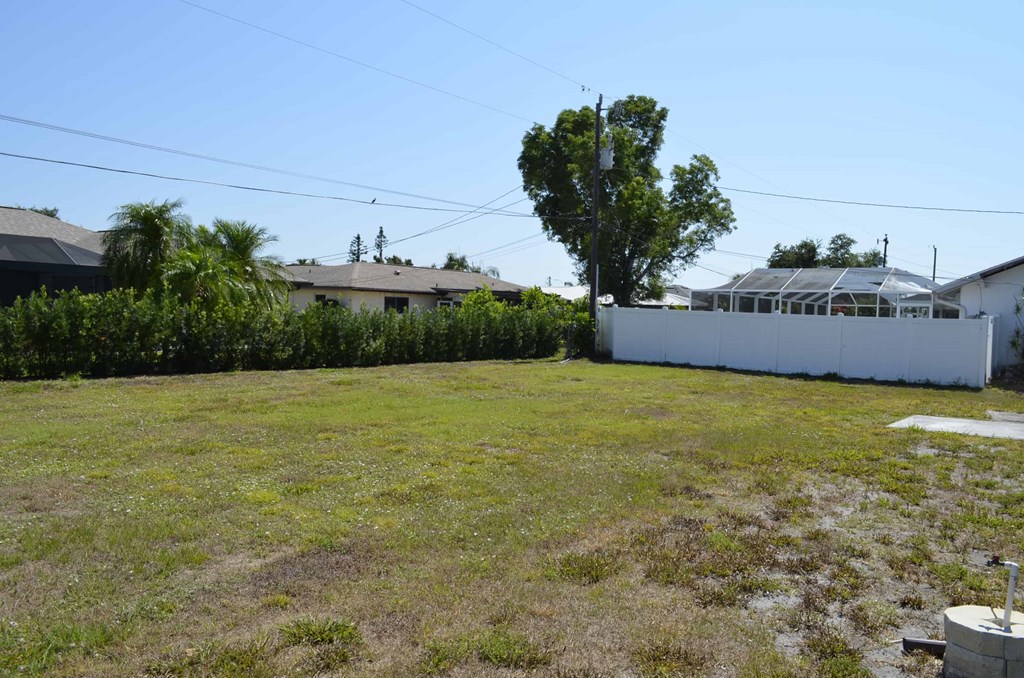 a yard with a white fence and houses in the background
