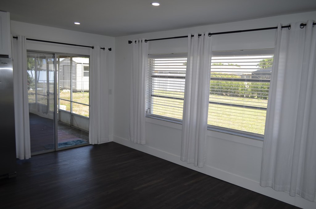 an empty living room with white curtains and a sliding glass door