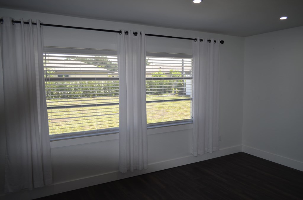 an empty living room with white curtains and a window with a view of a yard