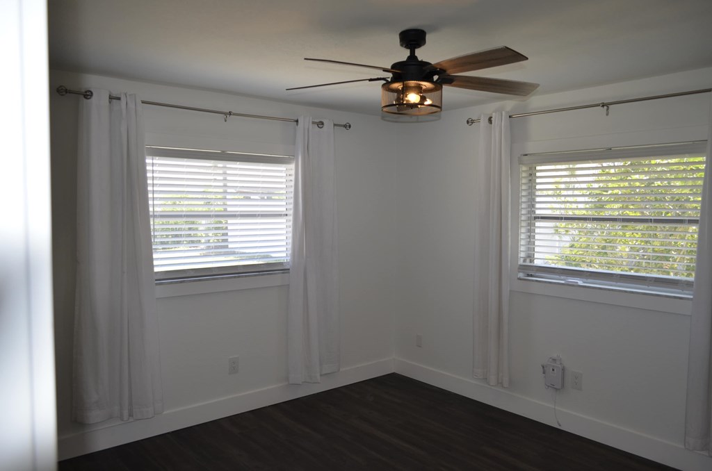 a bedroom with a ceiling fan and two windows