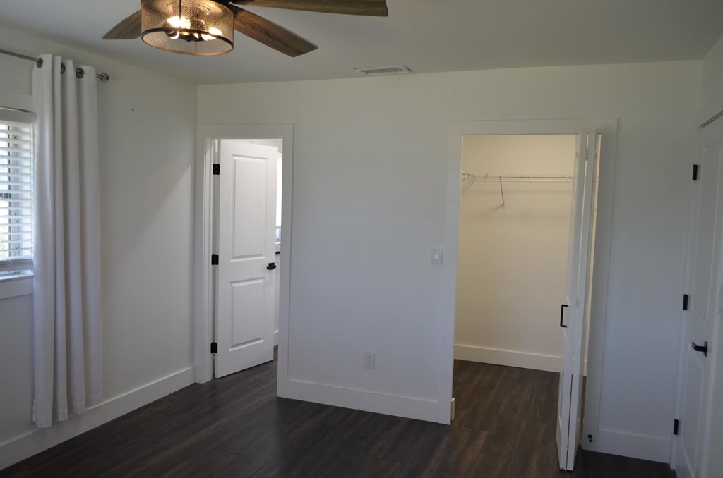 a bedroom with white walls and a closet and a ceiling fan