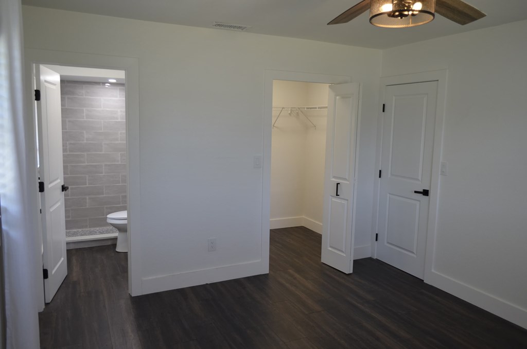 a bedroom with white walls and wood flooring and a door to a bathroom