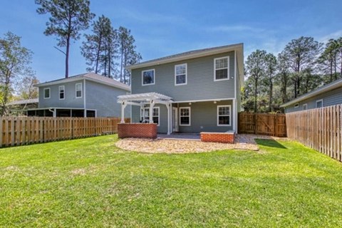 A house with a grey exterior and a white roof is surrounded by a wooden fence.