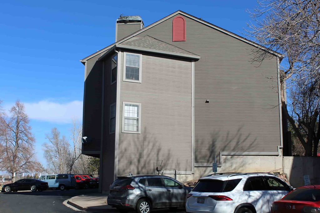 A grey building with a red window sill and cars parked in front.