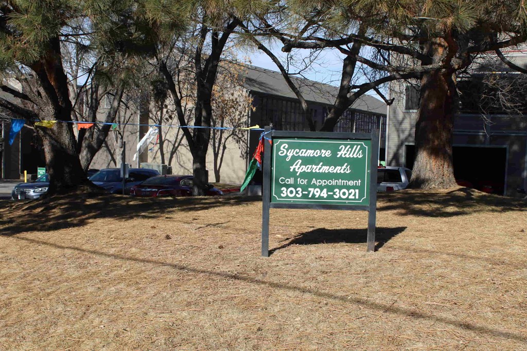 A sign for Sycamore Hills Apartments is displayed in a grassy area.