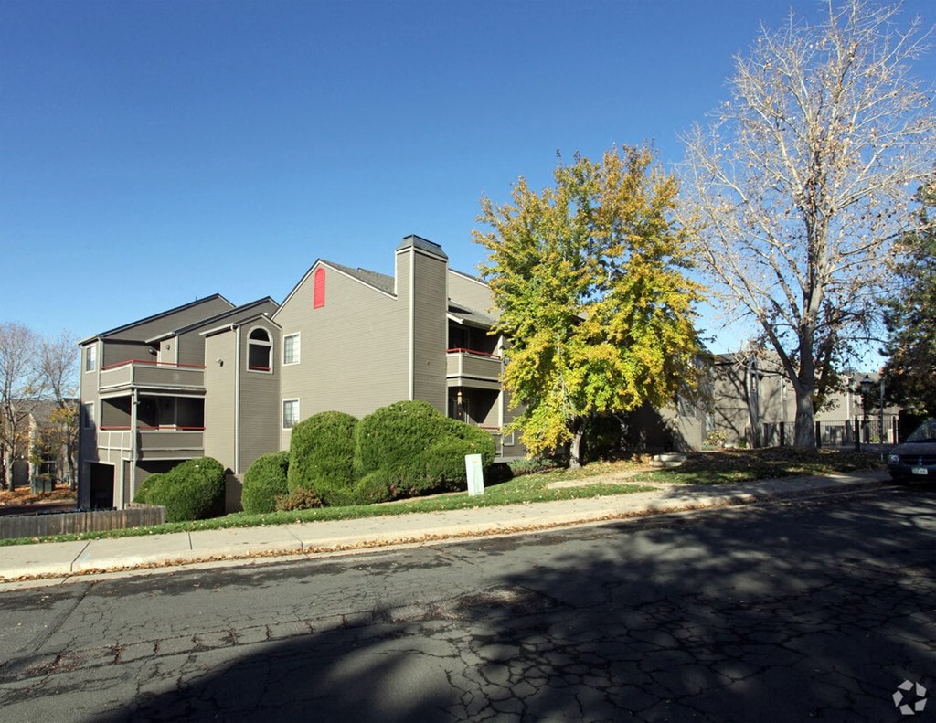 A grey building with a red roof is surrounded by trees and bushes.