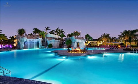 a resort pool with a waterfall and a fire pit at night