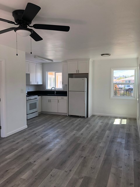 A kitchen with a fan and wooden floors.