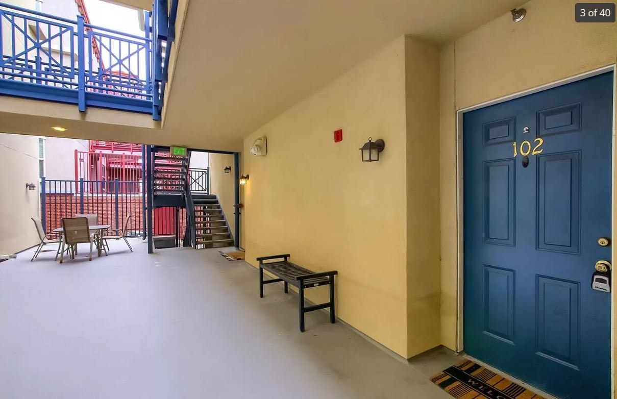 a room with a blue door and a balcony with chairs and tables