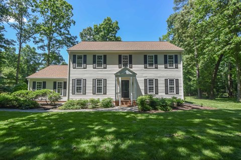 the front of a white house with green grass and trees