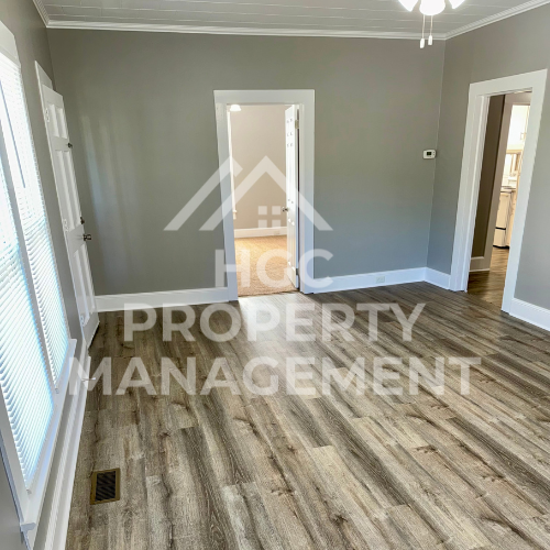 a renovated living room with hardwood floors and a door to a hallway