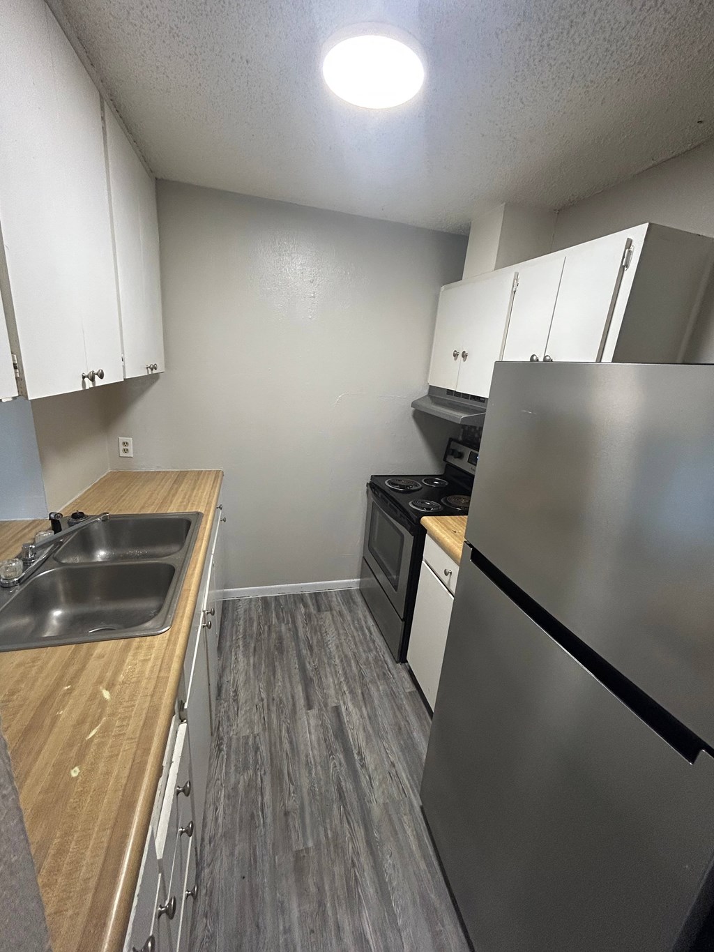 A kitchen with a stainless steel refrigerator, sink, and wooden countertops.
