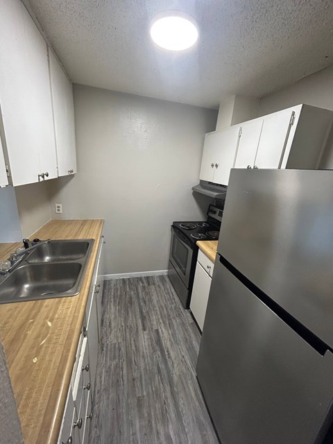A kitchen with a stainless steel refrigerator, sink, and wooden countertops.