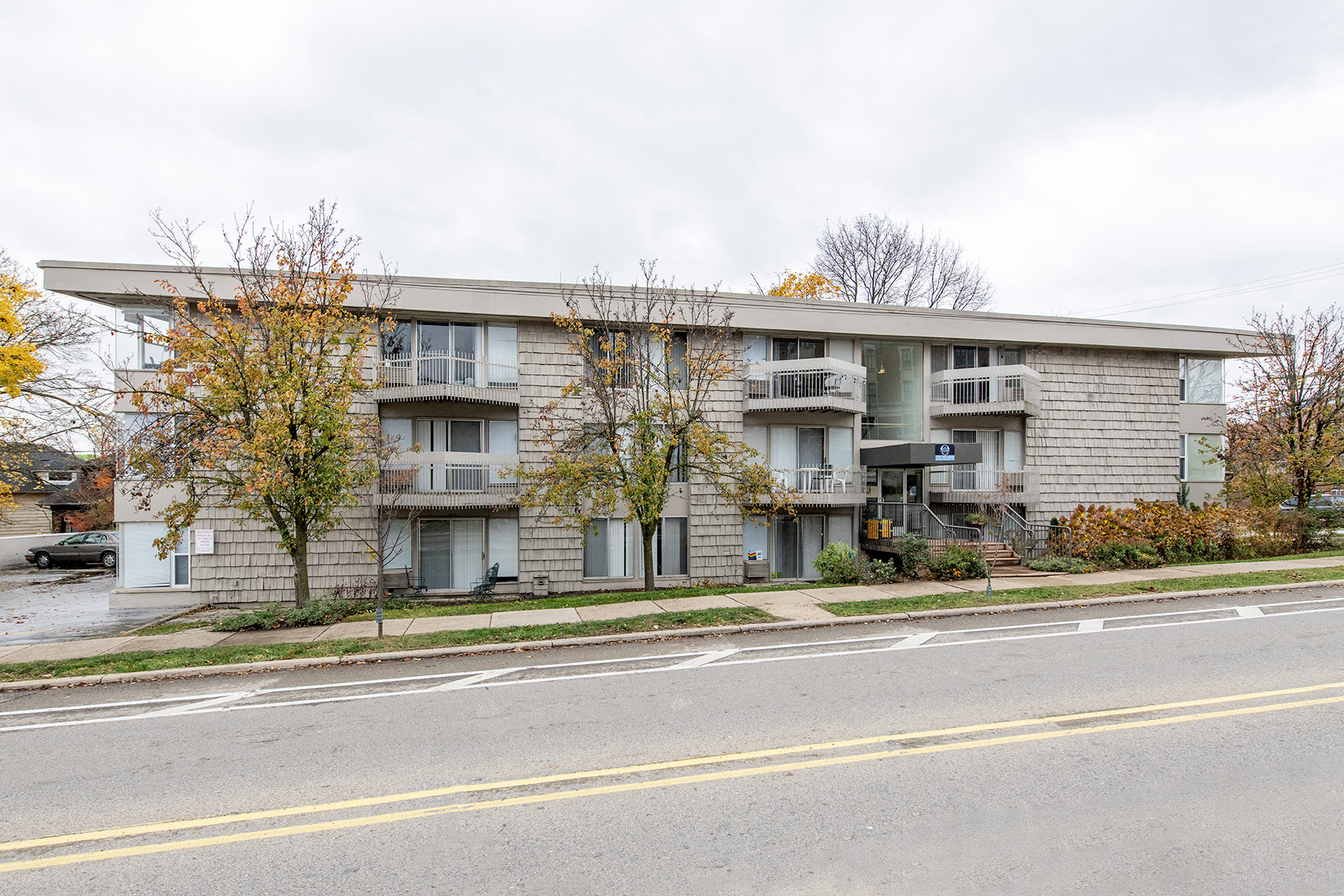 A grey apartment building with a car parked in front.