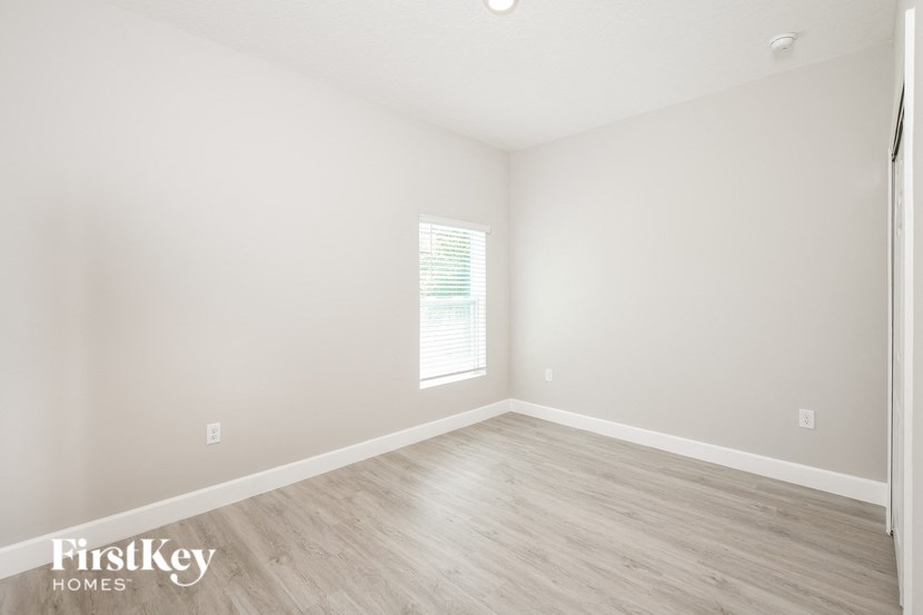 a bedroom with white walls and wood floors and a window