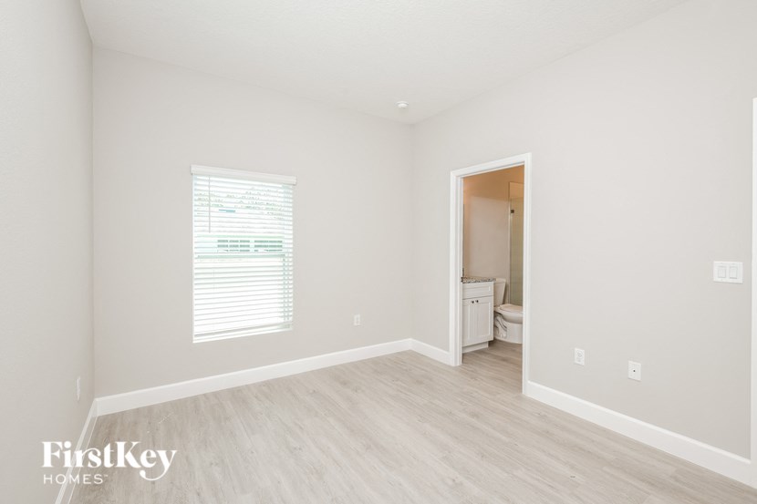 a bedroom with white walls and wood flooring and a bathroom