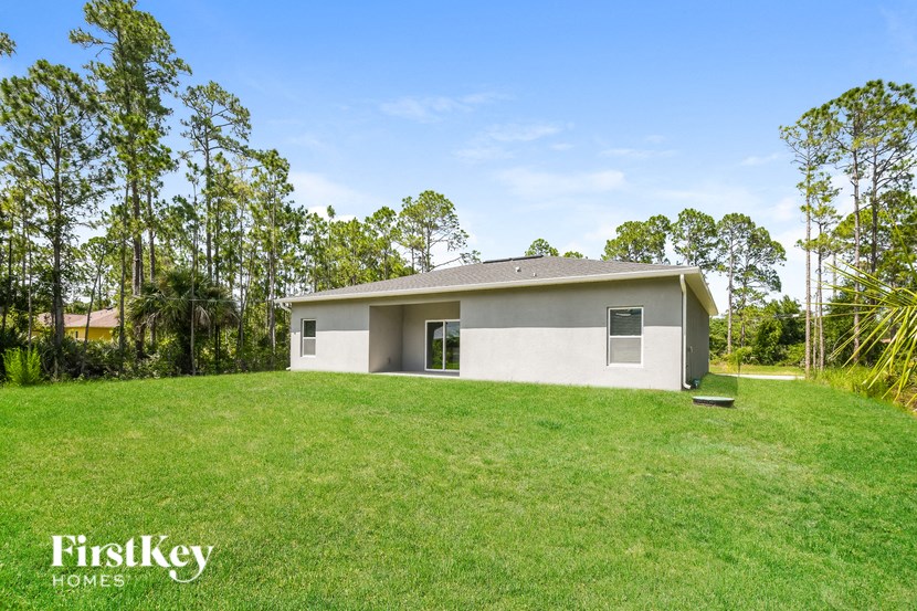 a small white house in a grassy yard with tall trees
