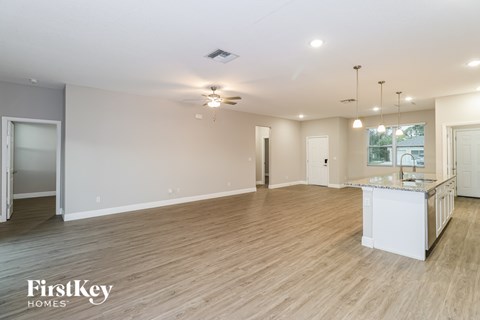 A spacious room with wooden flooring and a kitchen area in the background.