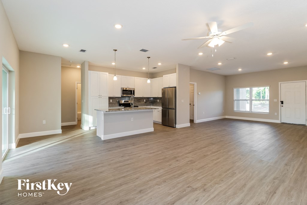 A spacious kitchen and living room with wooden floors and a ceiling fan.