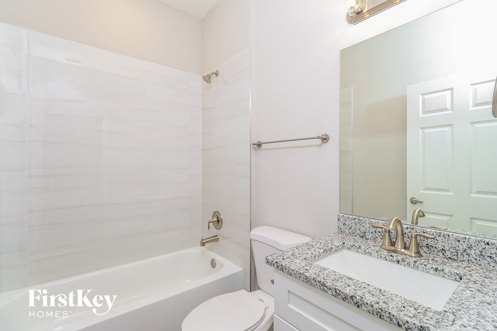 A white bathroom with a marble counter top and a white toilet.