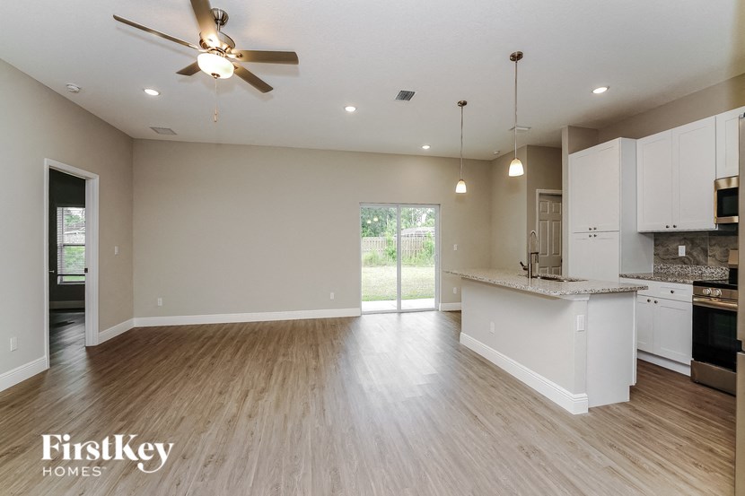 an empty living room with a kitchen and a ceiling fan