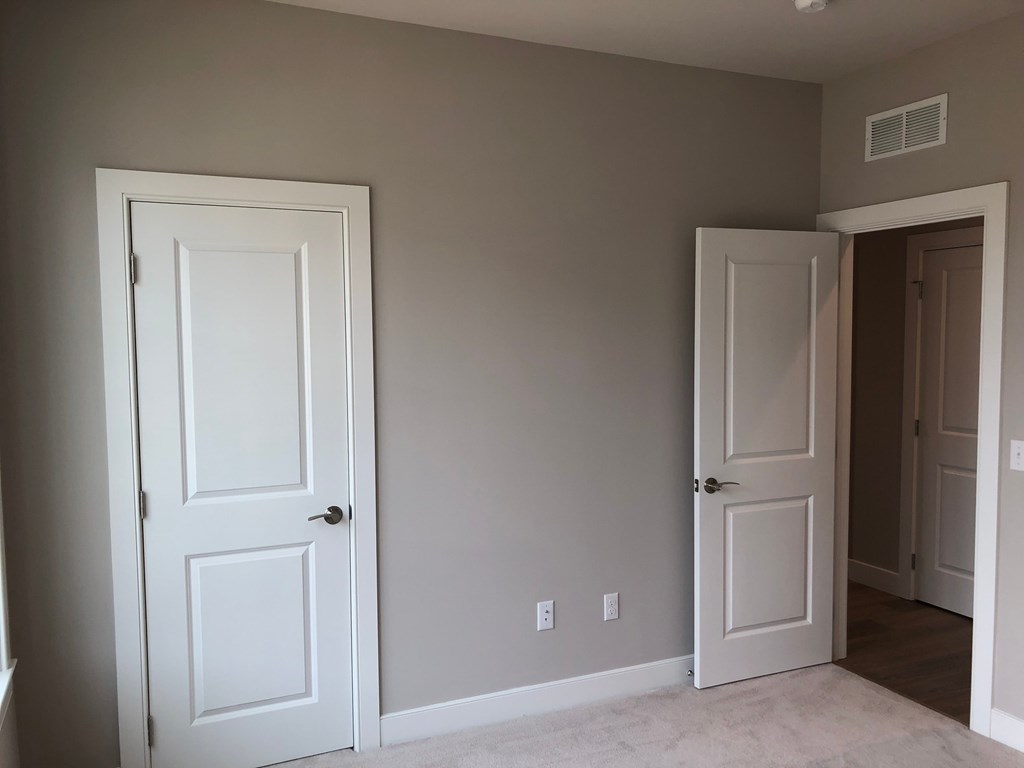 a bedroom with two white doors and a hallway with a door open to a closet