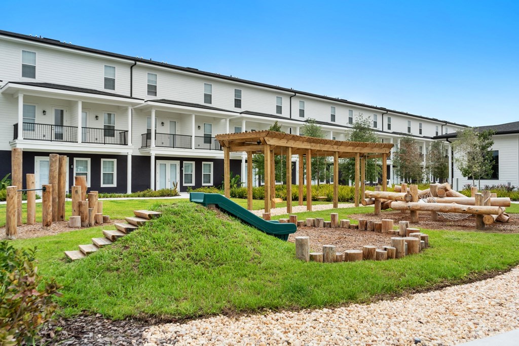 a playground with a slide and logs in front of an apartment building