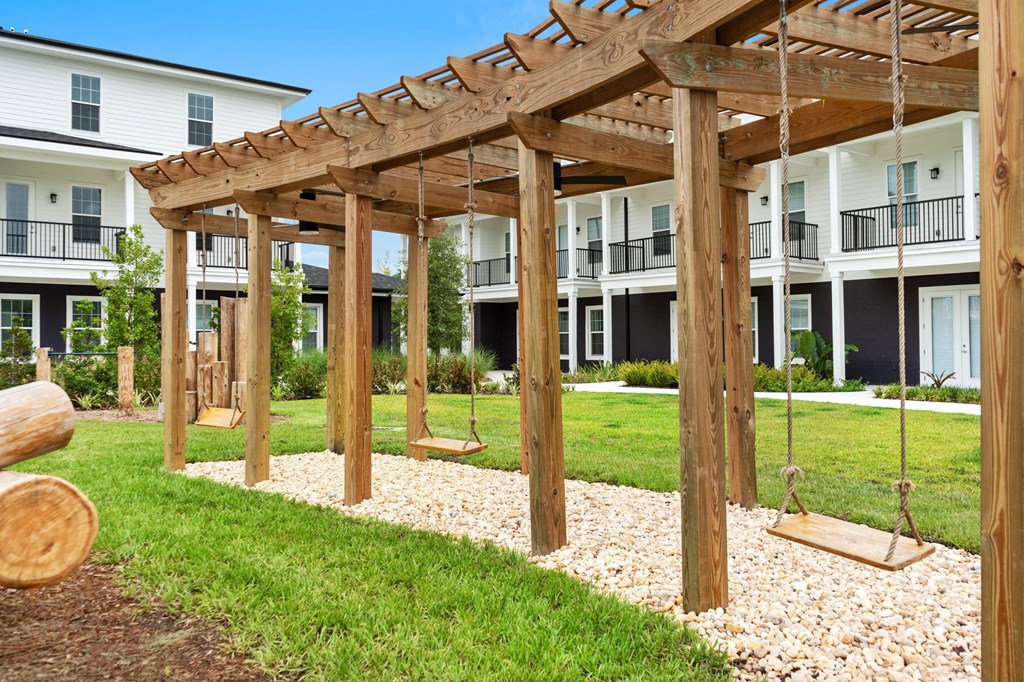 a playground with swings and a pergola in front of an apartment building