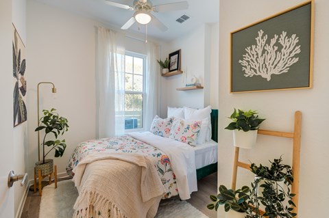 A bedroom with a bed, a plant, and a picture on the wall.