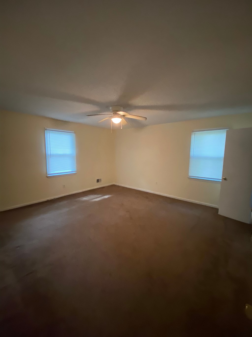 an empty room with a ceiling fan and two windows