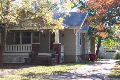 a yellow house with a white porch and trees