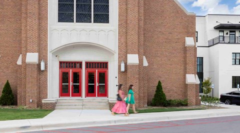 two women walking past a brick building with red doors