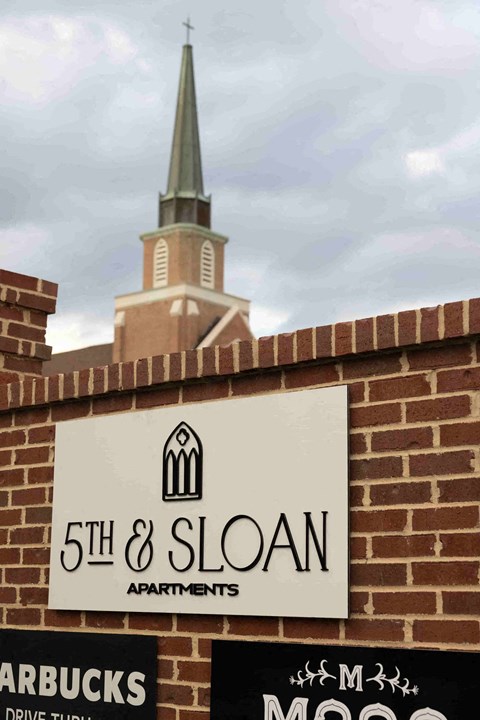 a sign for 5th  sloan apartments in front of a church steeple