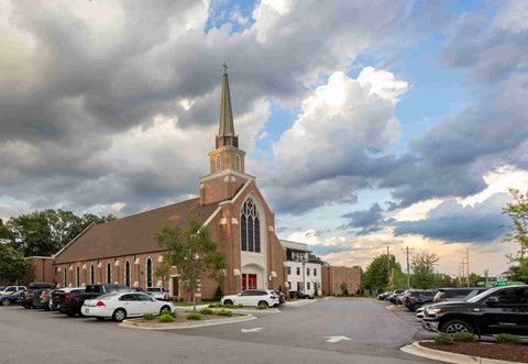 a church with a steeple and a parking lot with cars parked