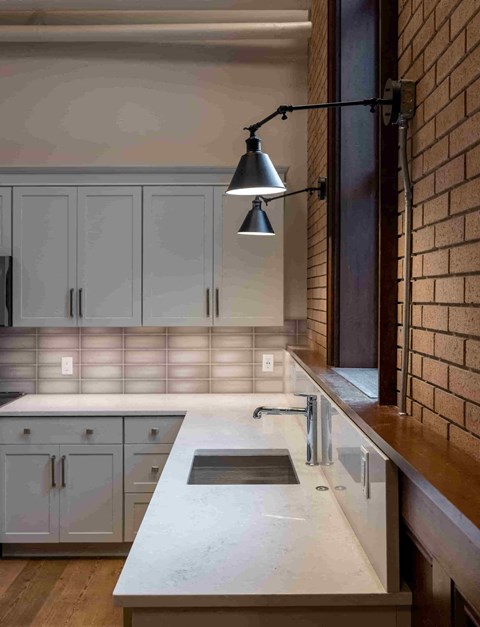 a kitchen with white cabinets and a sink and a exposed brick wall