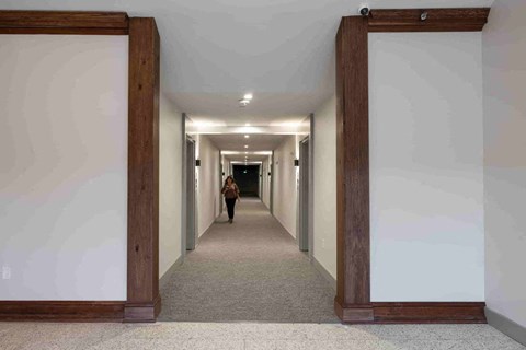a woman walking down a long hallway with open doors
