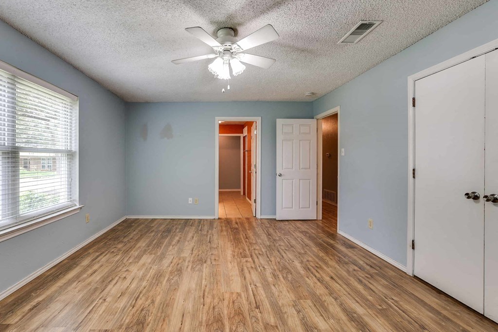 an empty living room with a ceiling fan and a door to a hallway